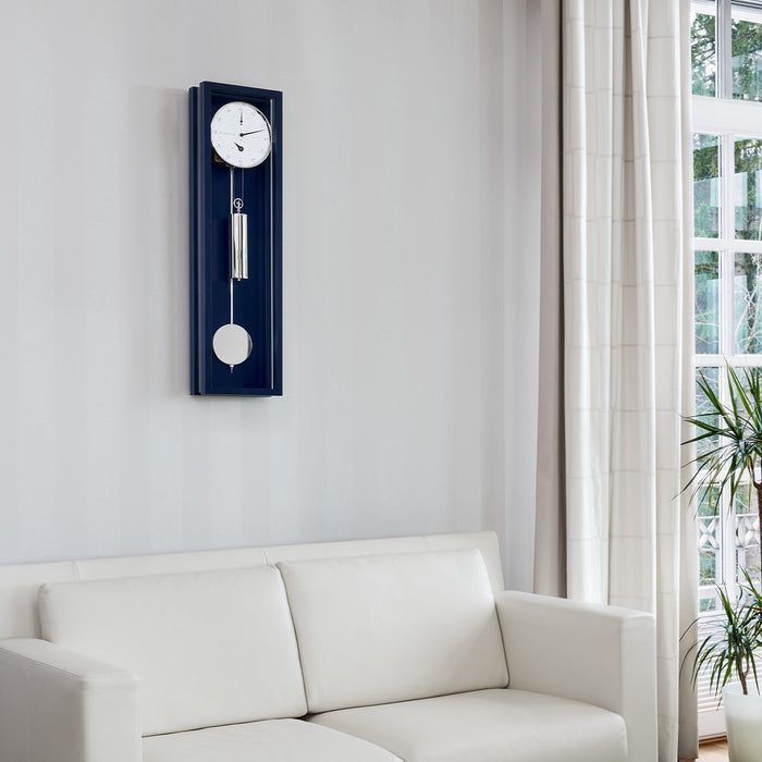 Blue wall clock hung above white couch in living room with plants on the side