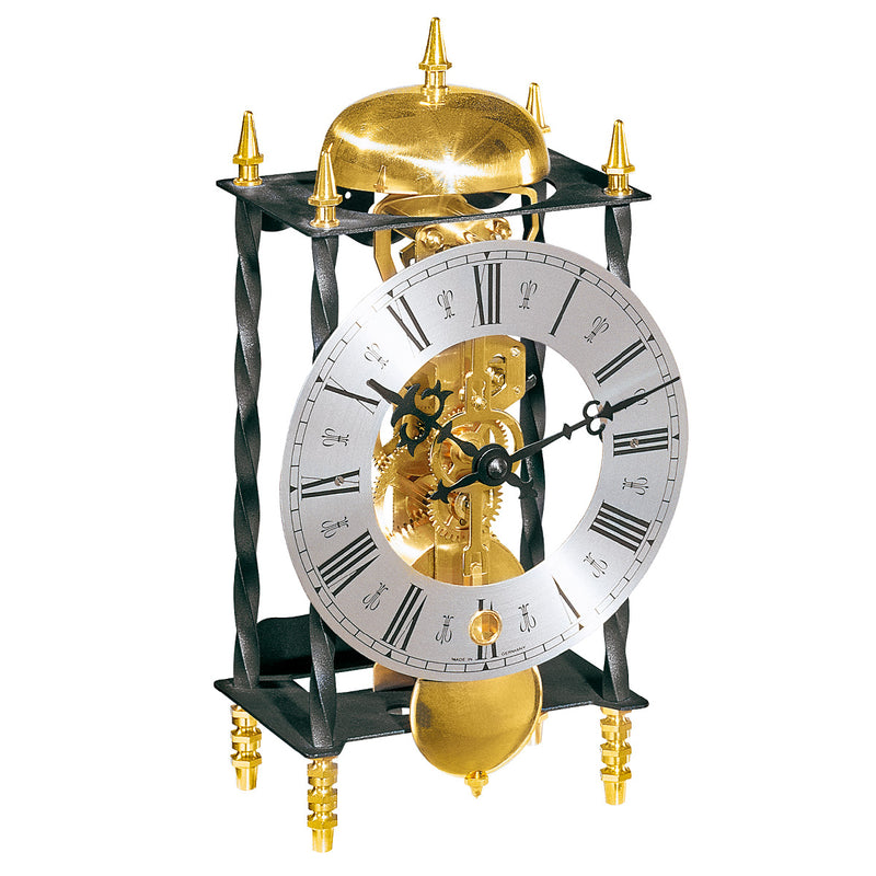 Decorative black metal clock with silver face and visible brass gears on white background.