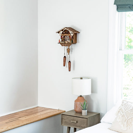 German cuckoo clock hanging on white wall above wooden nightstand with lamp