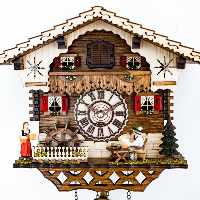 Up close German cuckoo clock with wooden roman numeral face and cottage style with figurines 