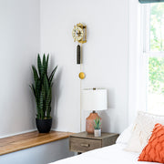 Brass skeleton clock hanging above green plant in bedroom.