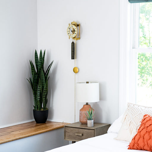 Brass skeleton clock hanging above green plant in bedroom.