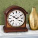 Wooden barrister style, vintage look,  mantel clock on marble mantel next to golden vase with floral pattern wall in background