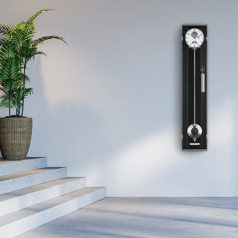 Wall clock with pendulum on a light gray wall next to a staircase with a plant.