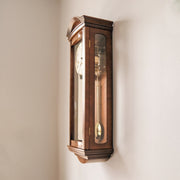 Side view of wooden wall clock with glass panes hanging on white wall