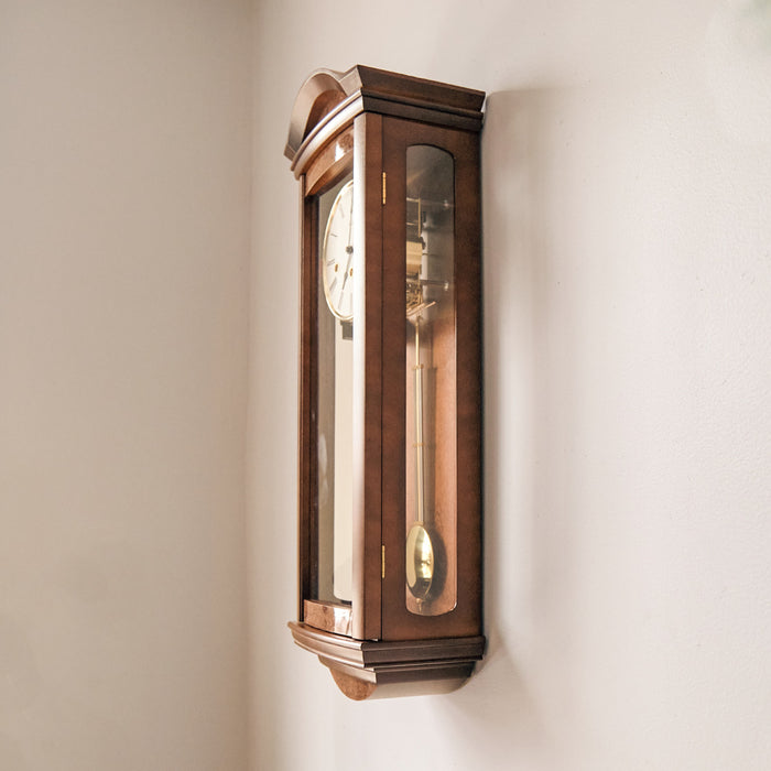 Side view of wooden wall clock with glass panes hanging on white wall