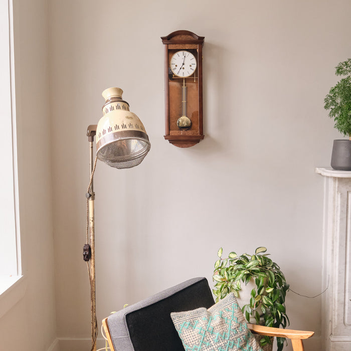 Wooden wall clock hanging on living room wall above chair and floor lamp