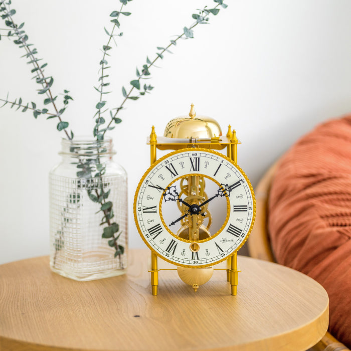 Brass clock sitting on wood table with plant and soft chair in background 