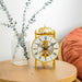 Brass clock sitting on wood table with plant and soft chair in background 