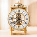 Brass mantel clock with intricate gears and bell on top sitting on white table