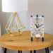 Silver and blue mechanical clock with glass face on wood table next to gold lamp