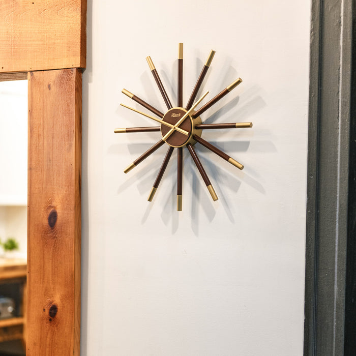 Sunburst style wooden clock hanging on white wall next to doorway.
