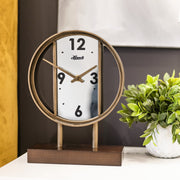 Decorative desk clock with mirrored face sitting on white marble tabletop next to green plant. 