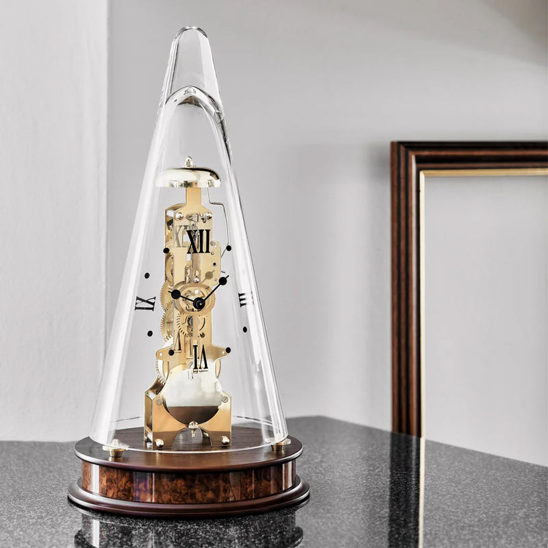 Decorative clock under a glass dome on a marble countertop with a white wall in the background