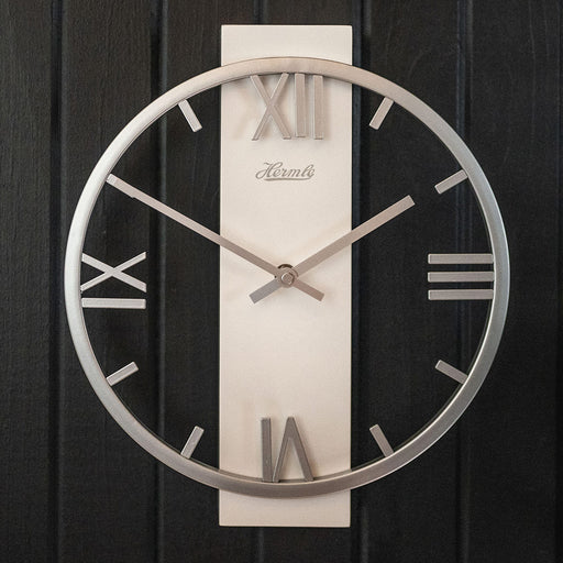 Metal clock with roman numerals and open frame design hanging on black plank wall.