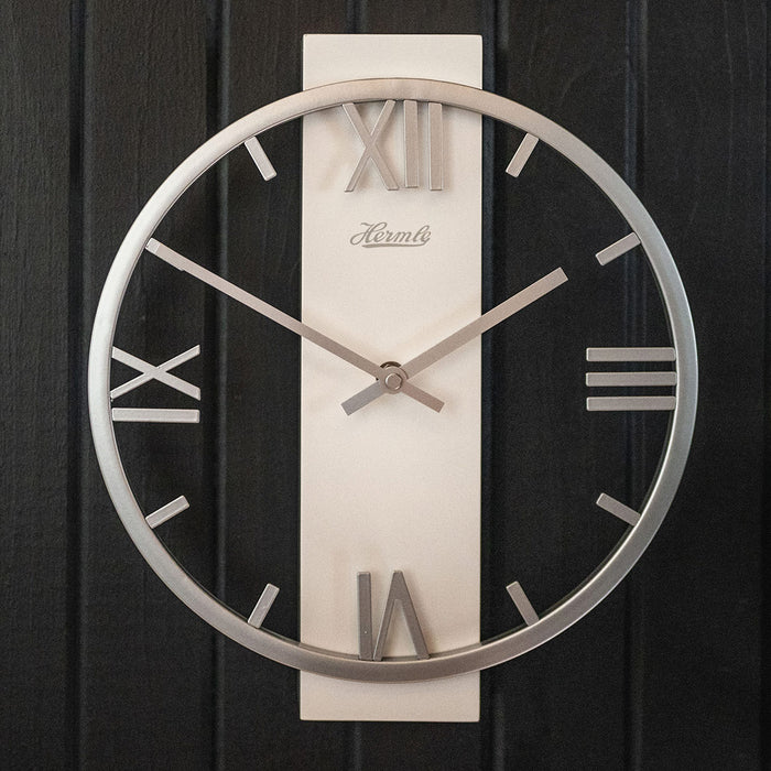 Metal clock with roman numerals and open frame design hanging on black plank wall.