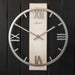 Metal clock with roman numerals and open frame design hanging on black plank wall.