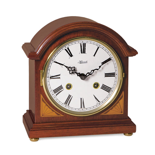 Cherry wood mantel clock with brass highlights and roman numeral face on white background.
