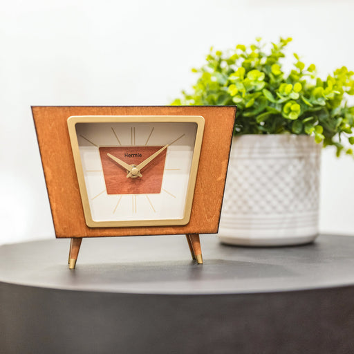 Retro style desk clock on gray side table in front of green plant. 