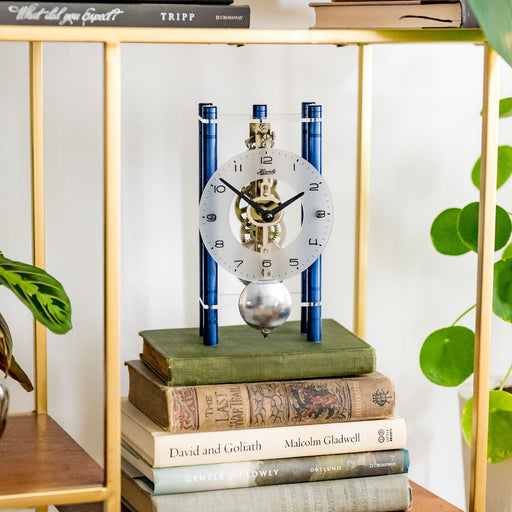 Blue and silver clock sitting on stack of books next to potted plants 