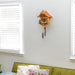 Wooden cuckoo clock on a white wall above a green sofa with cushions.