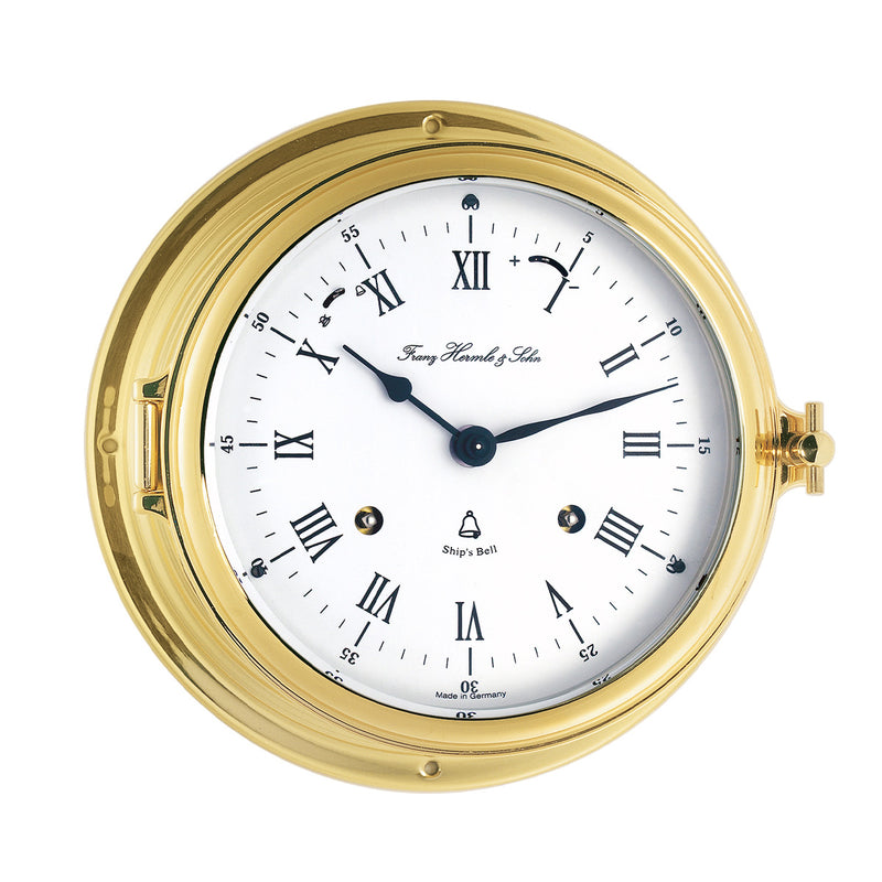 Brass ship's clock with roman numeral face and holes for winding mechanical movement inside on white background.