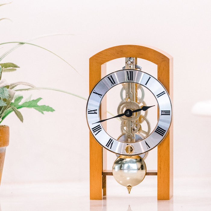 Light cherry mechanical clock on white table next to green plant
