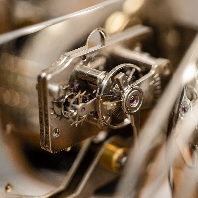 Up close of tourbillion with nickel finish and jewels mounted inside mechanical clock.