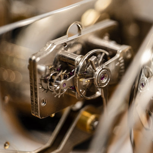 Up close of tourbillion with nickel finish and jewels mounted inside mechanical clock.