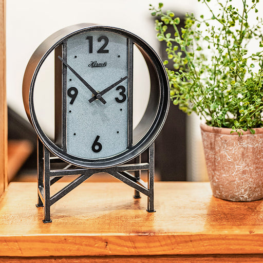 Wrought iron desk clock on wooden counter with rustic plant. 