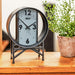 Wrought iron desk clock on wooden counter with rustic plant. 