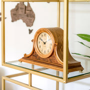 Light oak wood mantel clock on gold and glass shelf with world map behind.