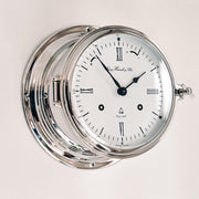 Close up angle view of silver finish Ship's Bell clock hanging on white wall.