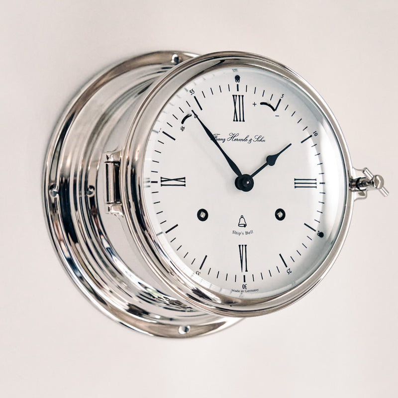 Close up angle view of silver finish Ship's Bell clock hanging on white wall.