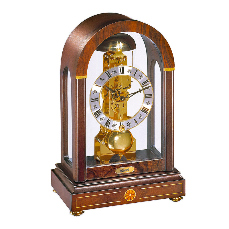 Wood mantel clock with arched glass panes and visible brass gears on white background.