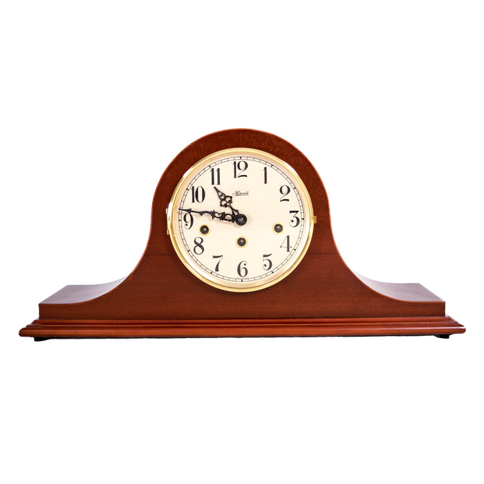 Wooden mantel clock with white face, brass highlights and holes for winding the mechanical movement on a white background.