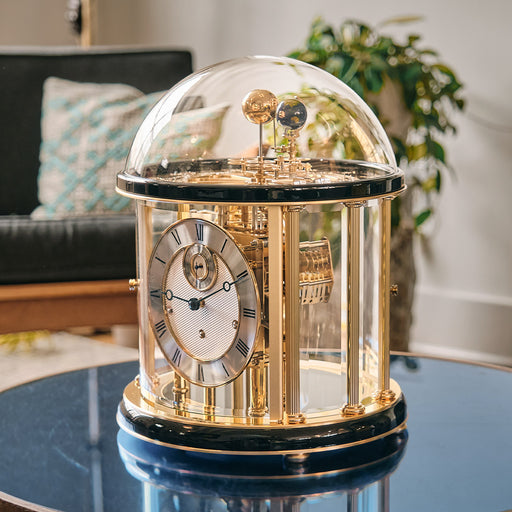Decorative Tellurium clock with a clear dome and intricate gears on a table in a living room setting