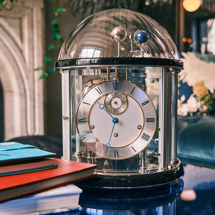 Black and silver Tellurium clock with glass dome in living room on blue table 
