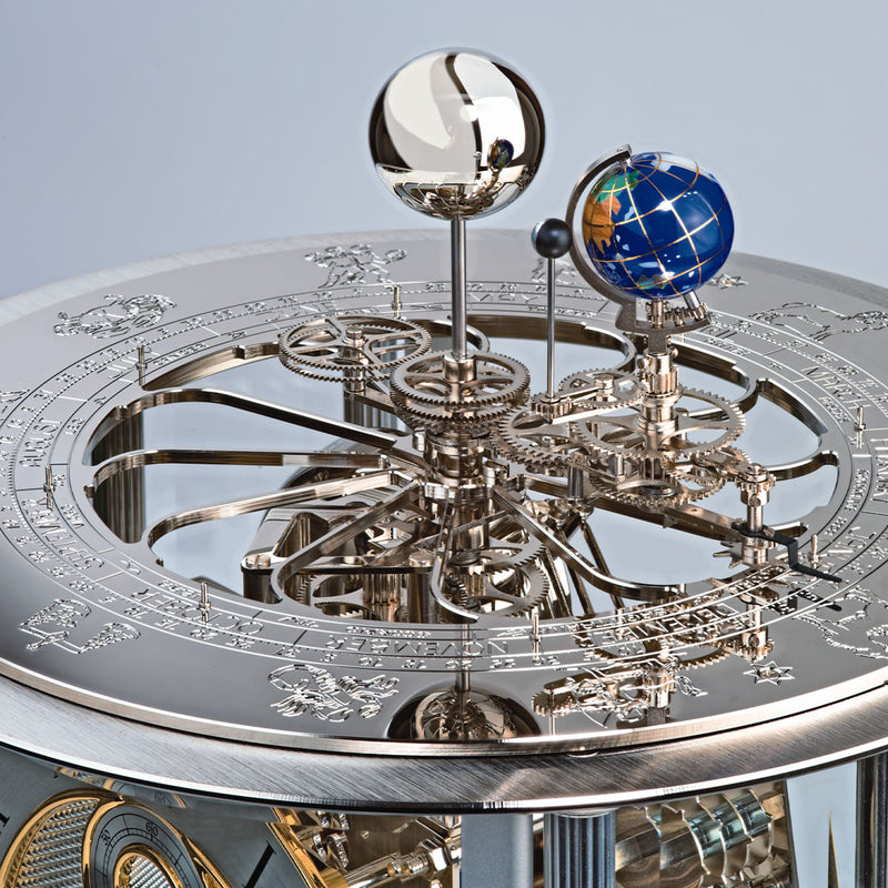 Close-up of a detailed mechanical clock with celestial globe on a light blue background
