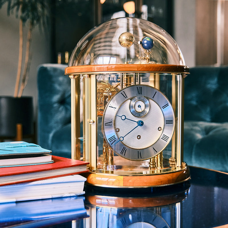 Cherry wood and brass Tellurium clock with glass in living room on blue table.
