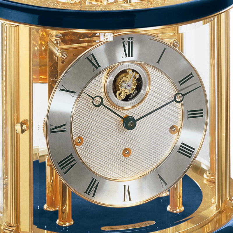 Up close of Tellurium clock face with silver color and roman numerals behind brass framed glass.