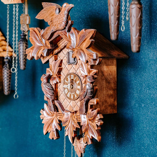 Cuckoo clock on blue wall surrounded by other cuckoo clocks