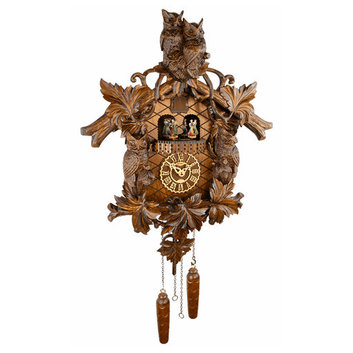 An ornate hand-carved wooden cuckoo clock featuring two owls at the top, leaf and bird motifs, a central clock face with Roman numerals, small figurines in the window, and two dangling wooden weights below, shown against a plain white background.