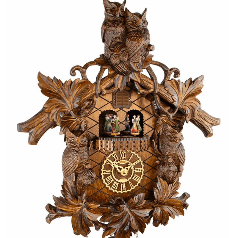 Close-up of ornate wooden cuckoo clock with owls and dancing figurines.