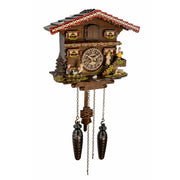 A traditional Black Forest cuckoo clock shaped like a mountain chalet, featuring a detailed clock face, small figurines, and two dark metal pendulums hanging below, shown against a plain white background.