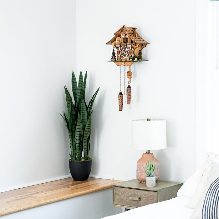 Wooden cuckoo clock on a wall above a wooden shelf with a potted plant and lamp.