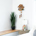 Wooden cuckoo clock on a wall above a wooden shelf with a potted plant and lamp.