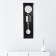 Black regulator wall clock hanging on white wall above white dresser