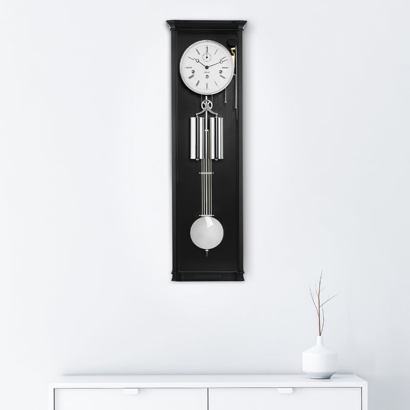Black regulator wall clock hanging on white wall above white dresser